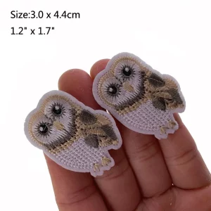 Two owl embroidered appliques in a person's hand.