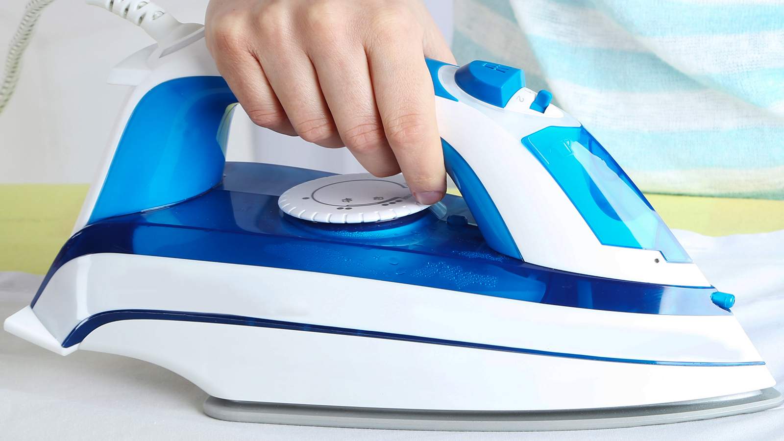 A person is ironing a shirt with a blue and white iron.