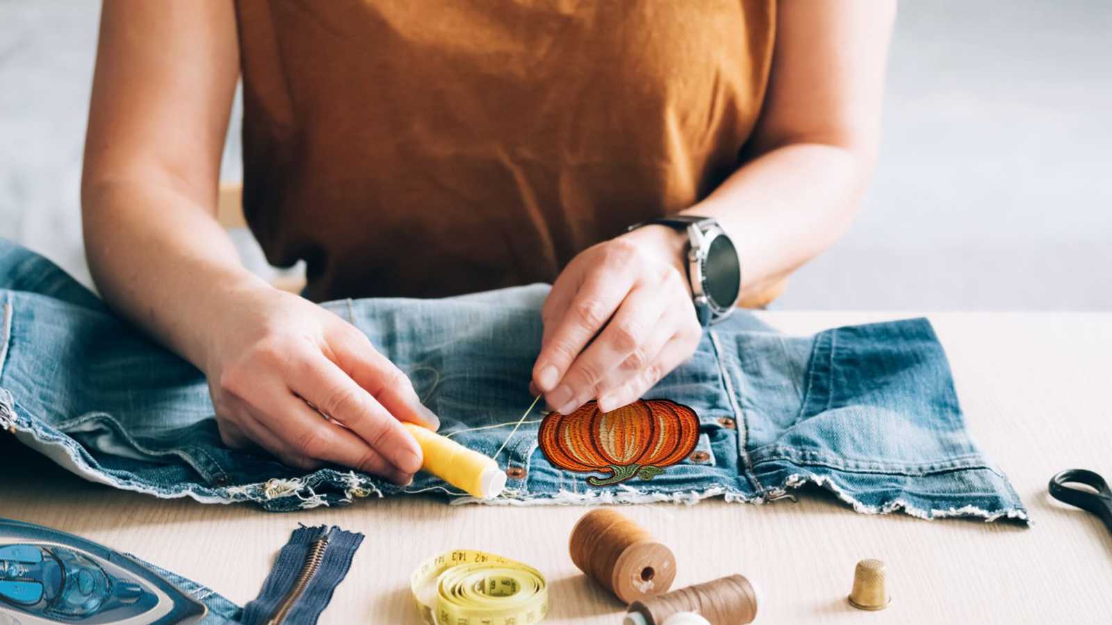 A woman is sewing a pair of jeans on a table.